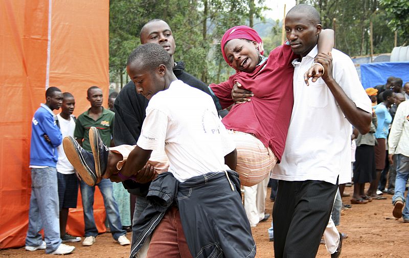 Relatives assist a distressed victim of the genocide at a mass-grave site in Kigali