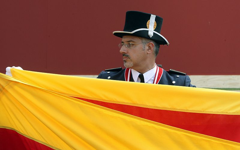 Un agente de los Mossos vestido de uniforme de gala pliega la senyera al término del acto.