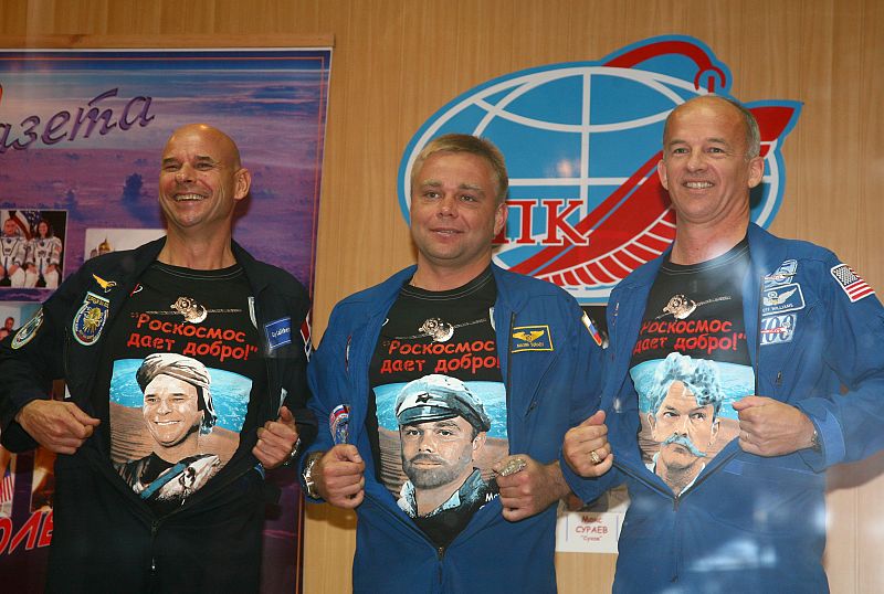 Los tres tripulantes muestran sus camisetas con dibujos durante la rueda de prensa en el cosmódromo de Baikonour.