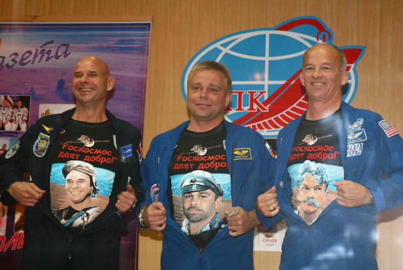 Los tres tripulantes muestran sus camisetas con dibujos durante la rueda de prensa en el cosmódromo de Baikonour. 