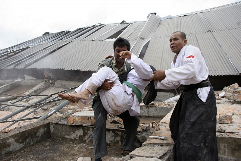 A man carries an injured person in front of a collapsed university building during an evacuation after an earthquake hit Padang