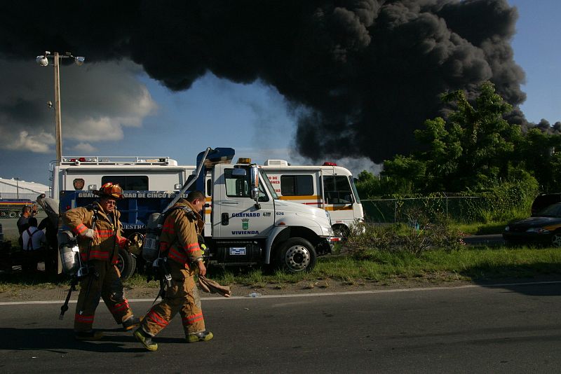 El cuerpo de Bomberos trabaja mientras se levanta una columna de humo debido al incendio de varios tanques de la refinería de petróleo de la empresa Caribbean Petroleum Corporation