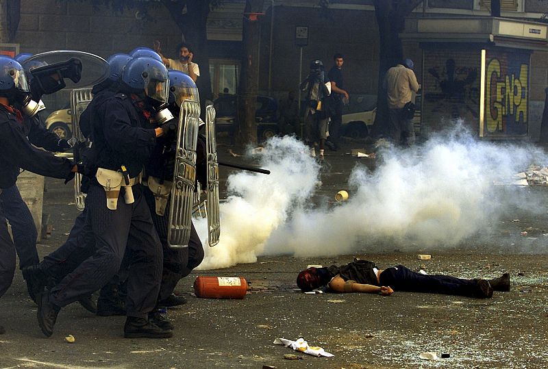 Riot police storm past a dead protestor who has been shot and killed by Carabiniere during rioting in central Genoa