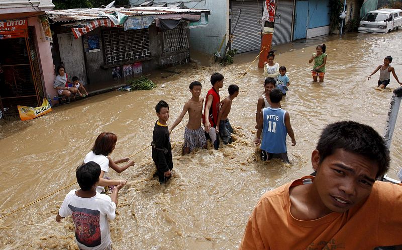 Un grupo de jóvenes atraviesan una calle completamente inundada tras el paso del tifón "Mirinae".