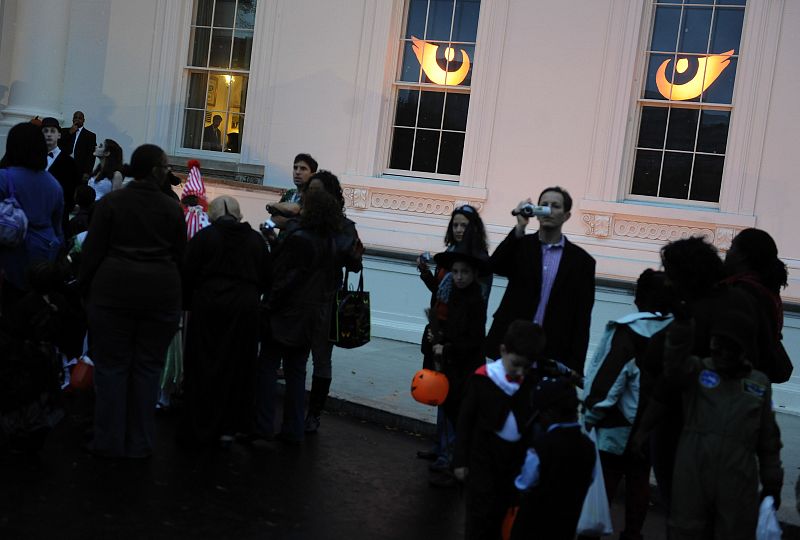 Windows of the White House glow like orange eyes as local school children wait in line at a Halloween reception by US President Obama and his family in Washington