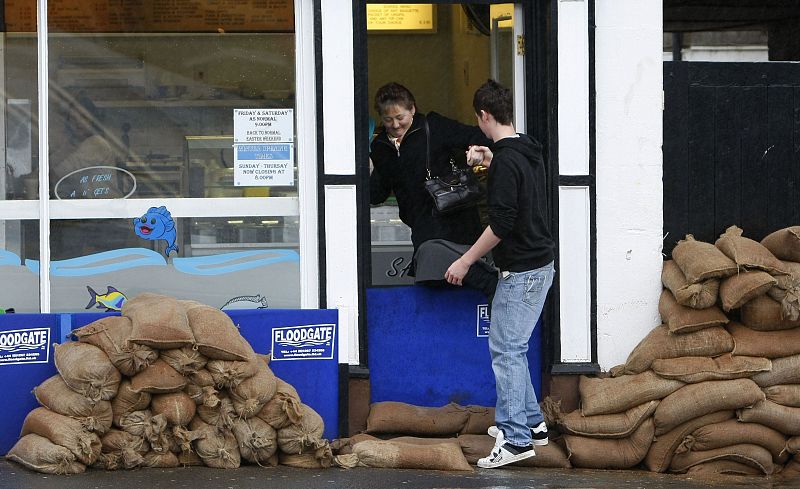 A woman is helped over a flood barrier in the village of Appleby