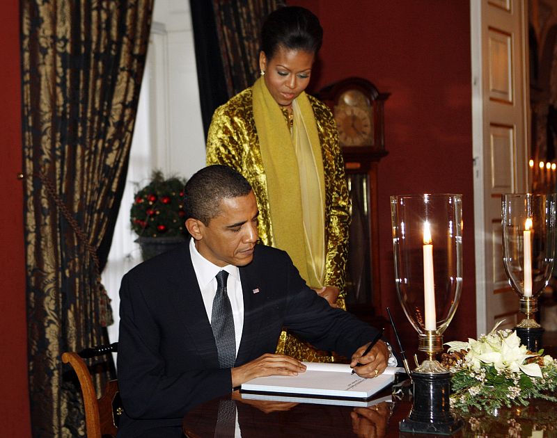 Barack Obama firma el libro de visitas del Palacio Real de Oslo bajo la atenta mirada de su esposa, Michelle.