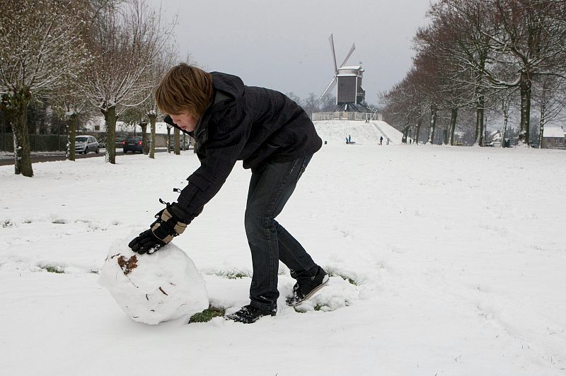 Un niño hace un muñeco de nieve en una plaza de Damme, en Bélgica.