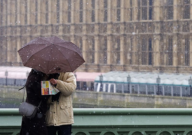 Una pareja se cobija bajo un paraguas de la ligera nieve que cae sobre Westminster y el Parlamento de Londres.