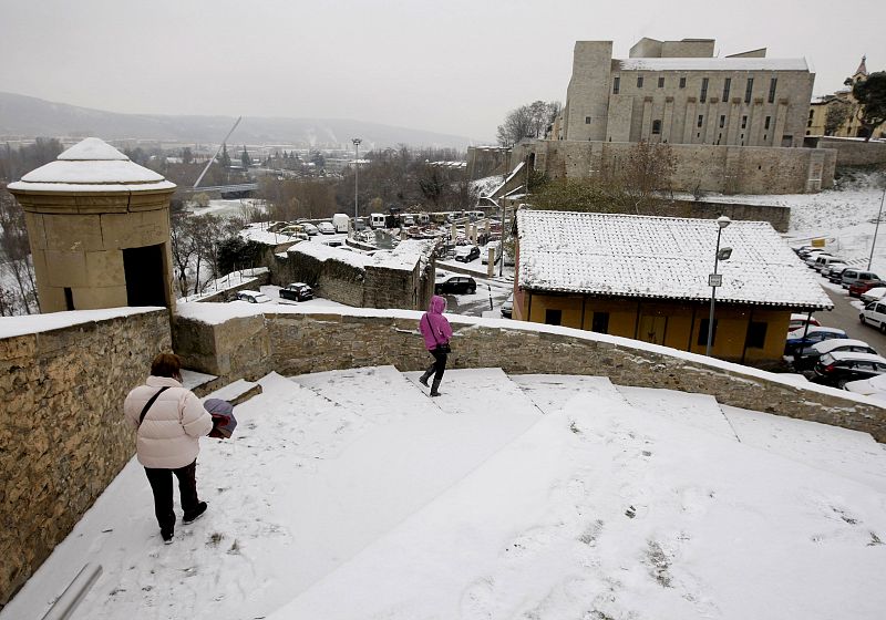 Dos mujeres descienden por unas escaleras cubiertas de nieve hacia la Cuesta de Santo Domingo de Pamplona.