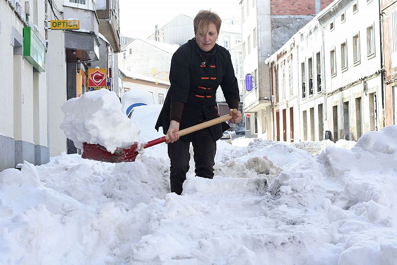 Una mujer retira con una pala la nieve acumulada en el acceso a su vivienda en Lugo.