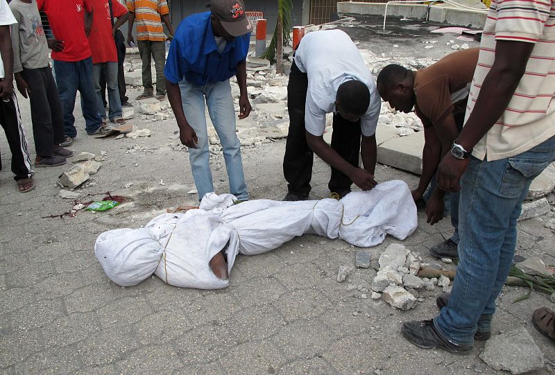 Haitians wrap of the body of an earthquake victim in Port-au-Prince