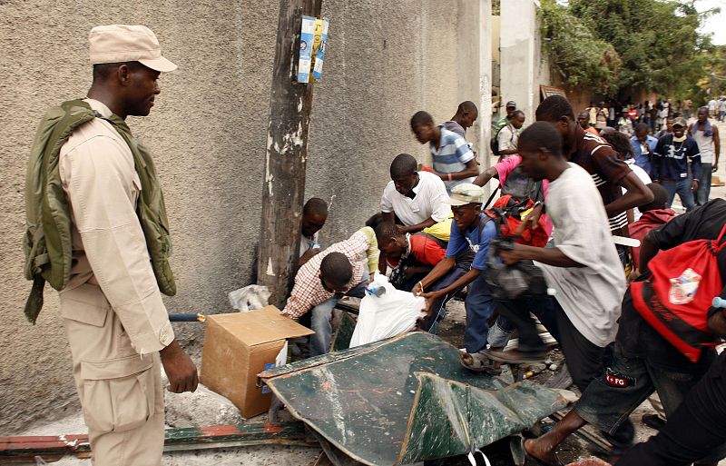 Residents fight for food as a police officer watches them after a major earthquake hit the Haitian capital Port-au-Prince