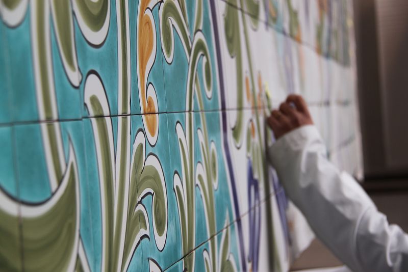 Uno de los pintores aplica color sobre el panel de azulejos.