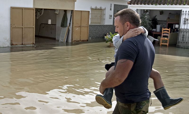 Un vecino del asentamiento jerezano de El Portal lleva en brazos a su hijo