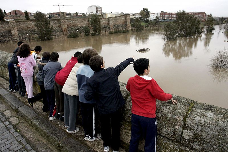 Unos niños observan desde el puente romano de Mérida la crecida del río Guadiana a su paso por la ciudad, que ha cubierto algunas zonas peatonales cercanas al cauce.