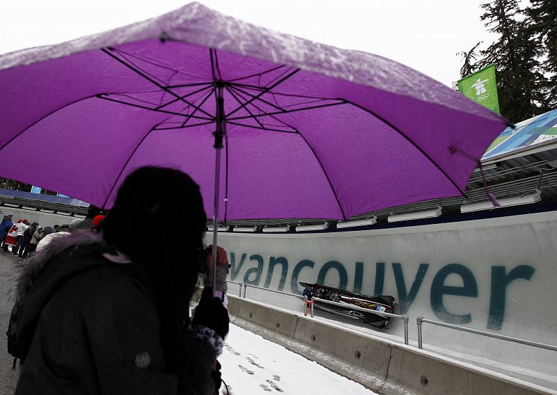 A spectator holding an umbrella watches team USA 1 of the four-man bobsleigh competition at the Vancouver 2010 Winter Olympics in Whistler