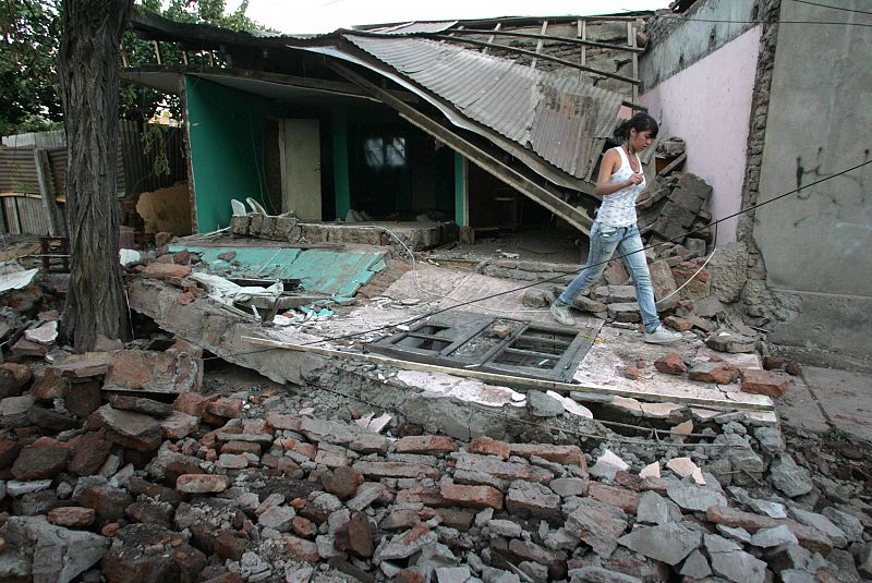 Una joven camina cerca a una vivienda destruida.