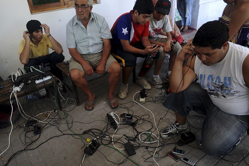 Varios  jóvenes chilenos cargan sus móviles en un punto de suministro de electricidad.