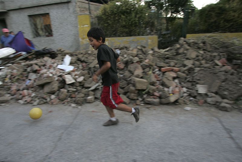 Un niño juega con una pelota cerca de las ruinas de una casa.