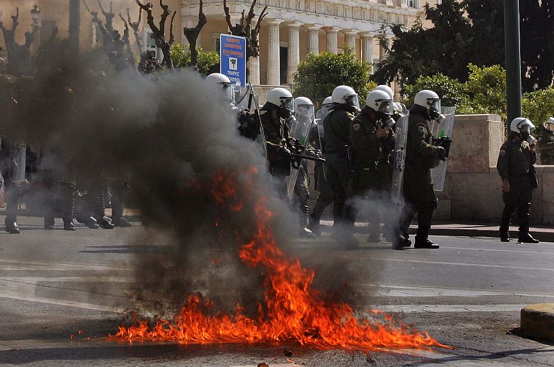 La policía antidisturbios hace guardia junto a un cóctel molotov lanzado por manifestantes frente al Parlamento.