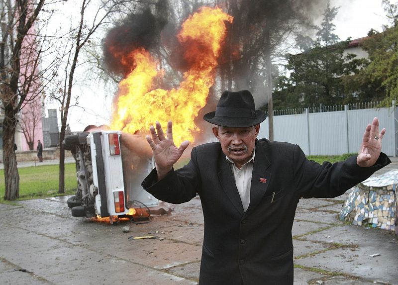 An anti-government protestor gestures in front of a burning car during clashes near the presidential administration in Bishkek