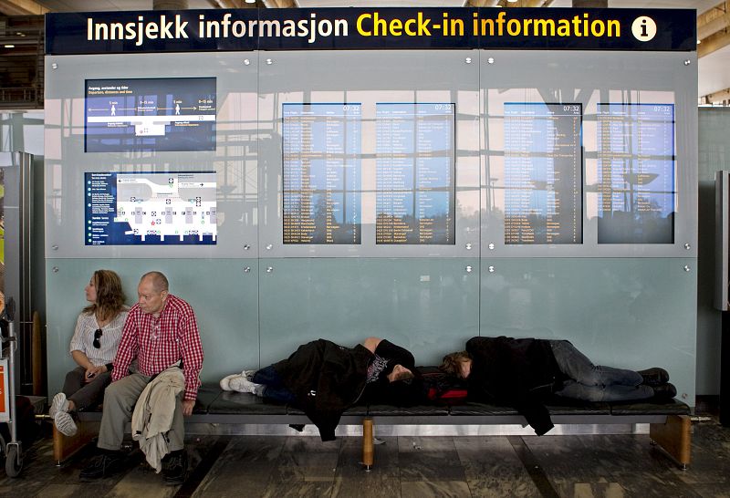 Varios viajeros descansan bajo los paneles informativos del aeropuerto Oslo tras conocerse la parálisis del tráfico  aéreo