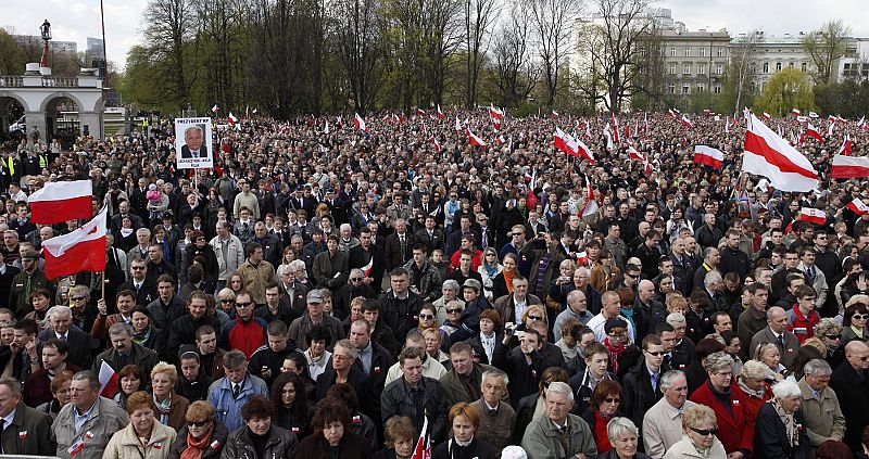 People hold flags as they wait for the start of a commemoration service for late Polish President Lech Kaczynski and other plane crash victims at the Pilsudski square in Warsaw