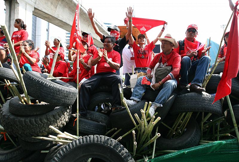 Varios "camisas rojas" permanecen sobre una barricada en frente de la policía tailandesa.