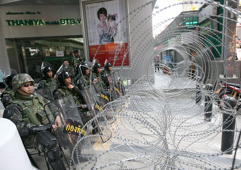 Soldados tailandeses vigilan delante de una alambrada cerca de una barricada.