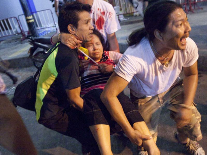 Men rush an injured woman to an ambulance after multiple explosions near pro-government supporters rallying in Bangkok