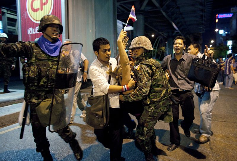 Army soldiers and a man assist an injured woman to an ambulance after multiple explosions near pro-government supporters rallying in Bangkok