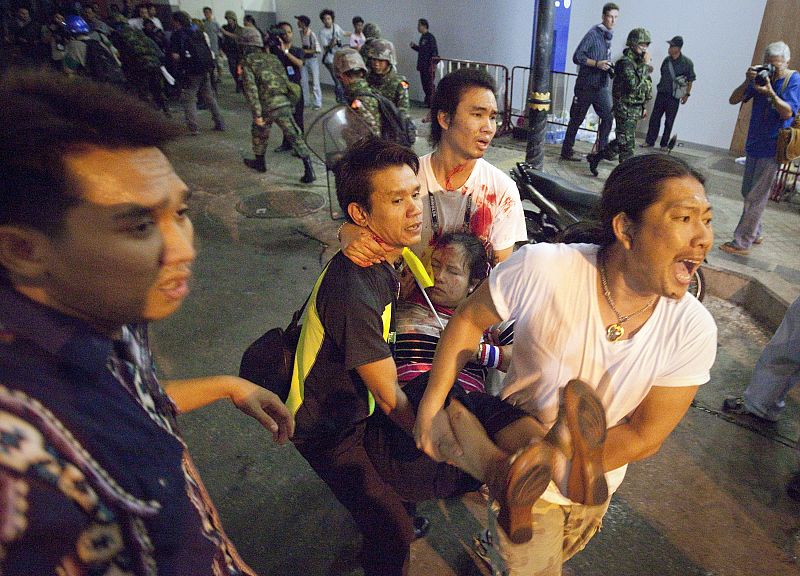Men rush an injured woman to an ambulance after an multiple explosions near pro-government supporters rallying in Bangkok's Silom business district