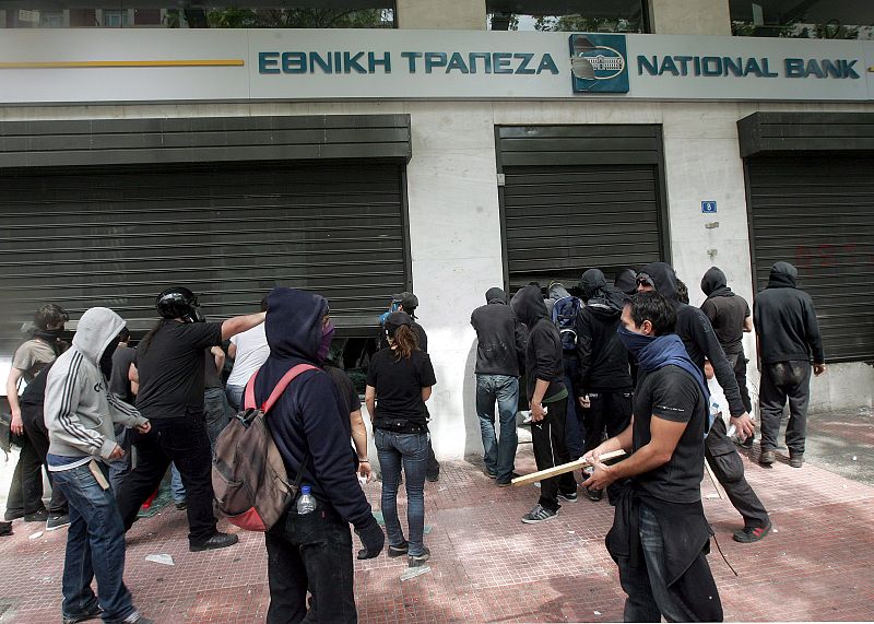 Varios manifestantes fuerzan los cierres de seguridad de una sucursal bancaria durante los disturbios que se están produciendo en esta jornada de huelga en Grecia.