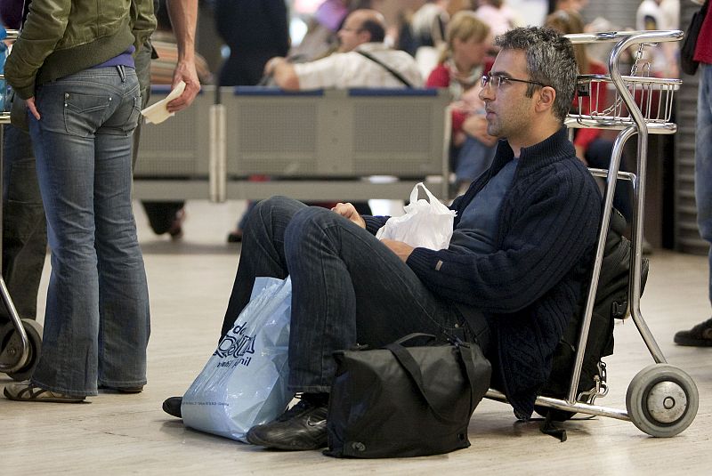 Un pasajero sentado sobre un carrito portaequipajes espera la reapertura del aeropuerto de Sevilla.