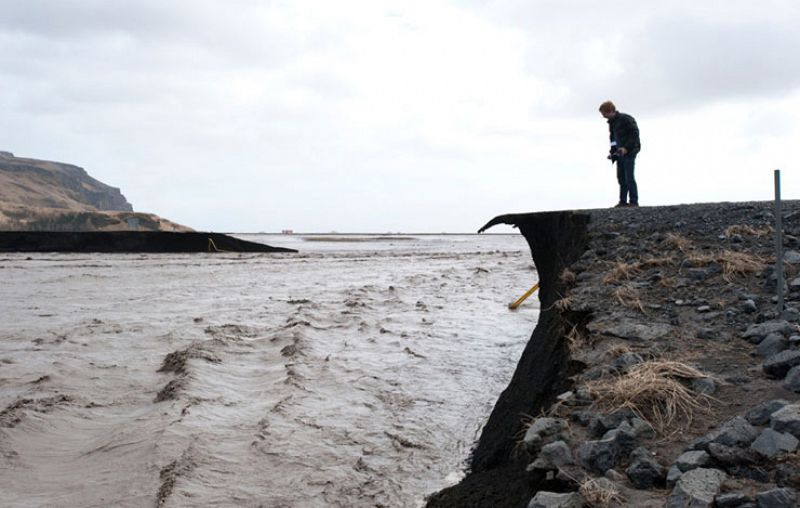 Un hombre toma una fotografía de una carretera inundada tras el deshielo del glaciar por la erupción del volcán.