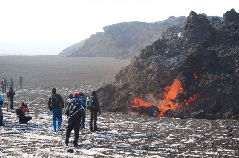 Varias personas se reúnen para ver el flujo de lava en el lugar de la erupción volcánica.
