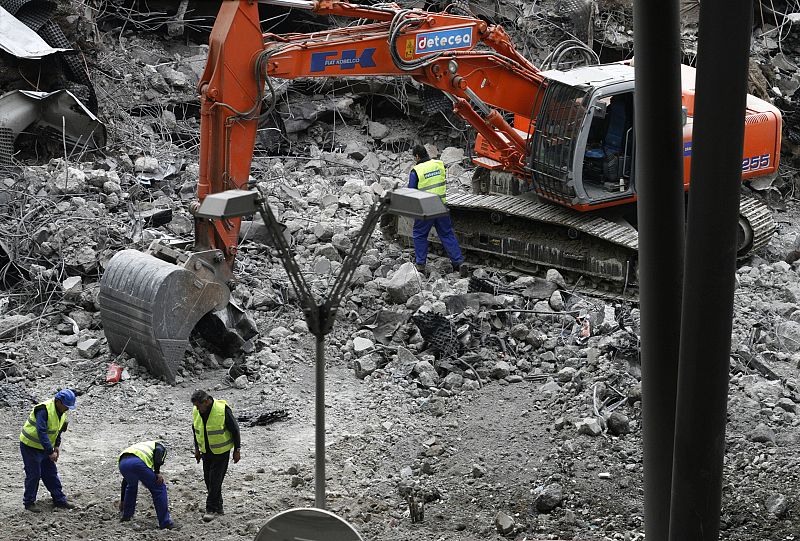 Workers remove debris after an explosion wrecked one of the parking lots of Madrid's Barajas airport