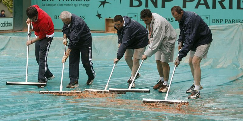 Los encargados del mantenimiento de las pistas de tenis quitan el agua de las cubiertas de lluvias tras un chaparrón.