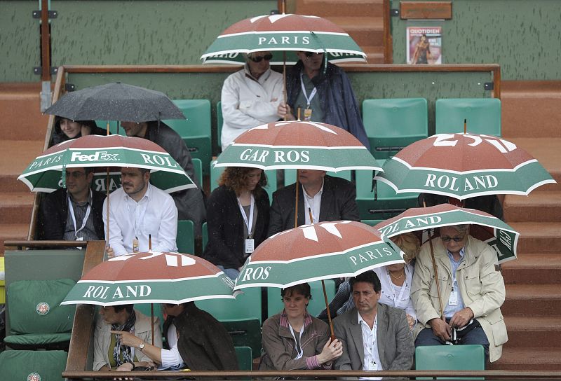 Los espectadores se protegen de la lluvia con paraguas durante el partido entre el tenista suizo Roger Federer y el colombiano Alejandro Falla.