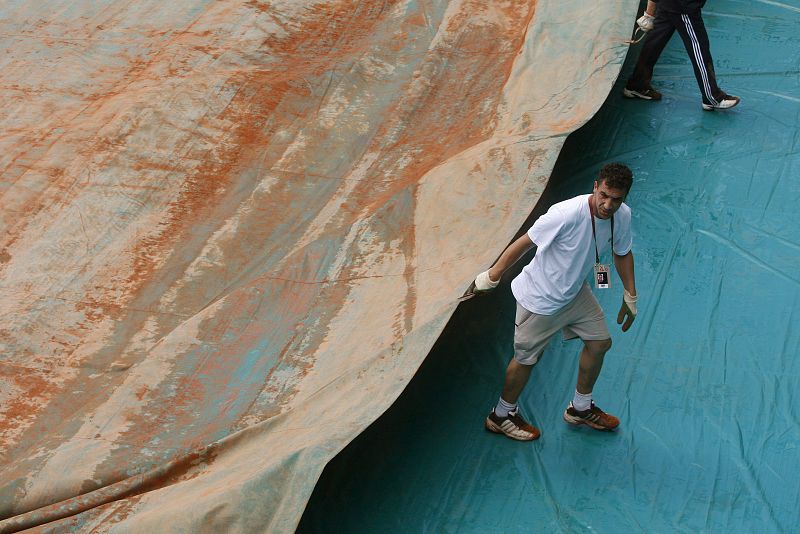Los encargados del mantenimiento de las pistas de tenis quitan las cubiertas de lluvias tras un chaparrón.