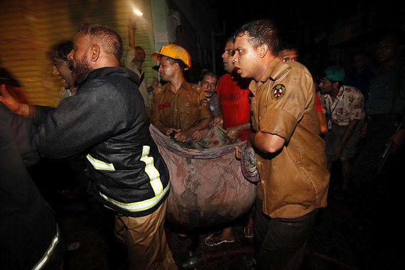 Locals and fire-fighters recover the body of a victim from the site of a fire in the old part of Dhaka