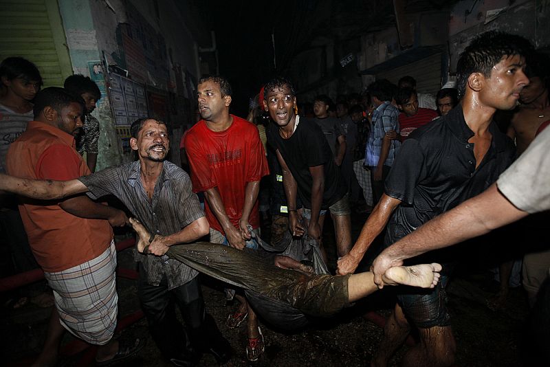 Locals and fire-fighters recover the body of a victim from the site of a fire in the old part of Dhaka