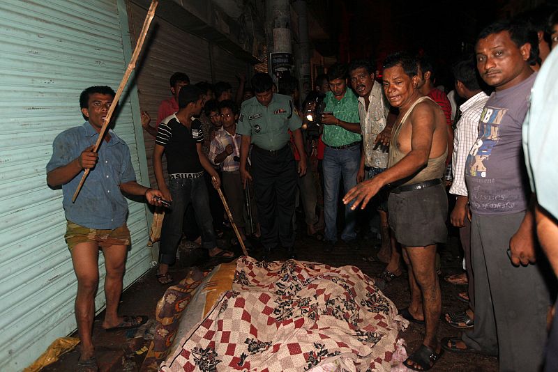 Locals and police officers stand around a pile of bodies recovered from the site of a fire in the old part of Dhaka