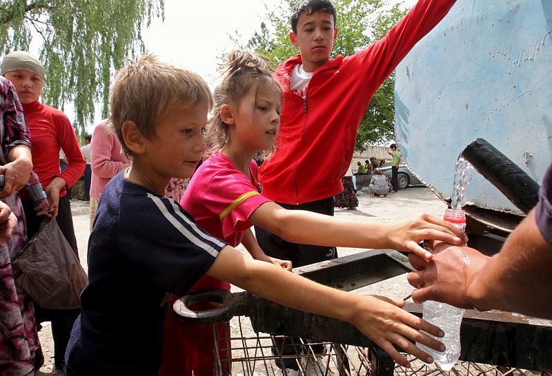 Niños uzbekos cogen agua en una fuente del campo de refugiados instalado junto a la frontera con Uzbekistán, a 7 kms del distrito uzbeko de Osh