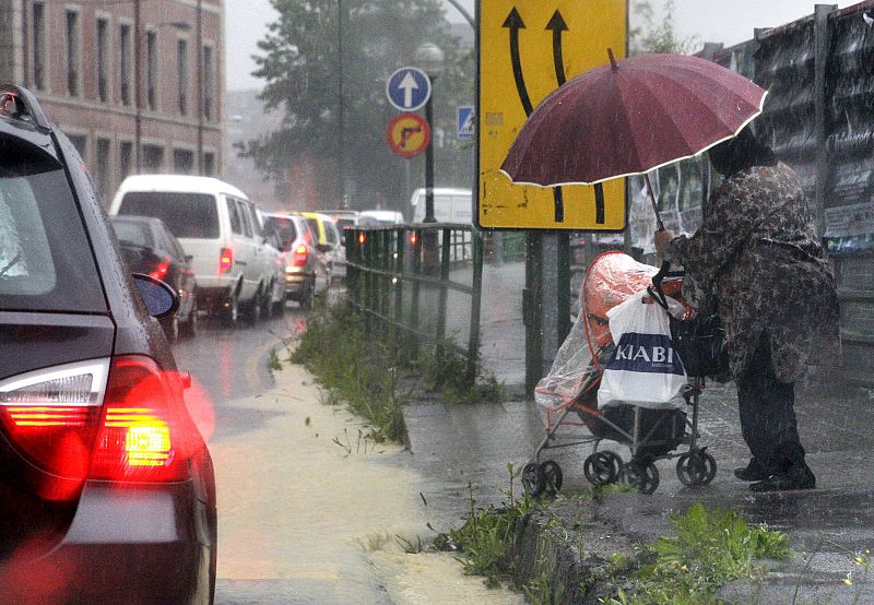 Una mujer intenta cruzar la calzada en Bilbao, donde las fuertes precipitaciones de las últimas horas están originando diversos problemas.
