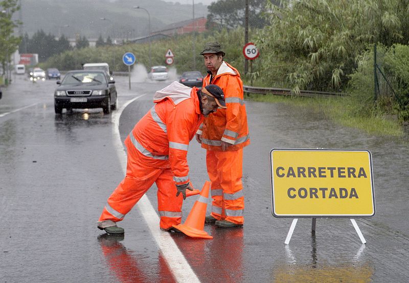 Dos operarios proceden a cortar la BI-735 a su paso por el municipio vizcaíno de Erandio debido a una gran balsa de agua commo consecuencia de las lluvias caídas en este territorio.