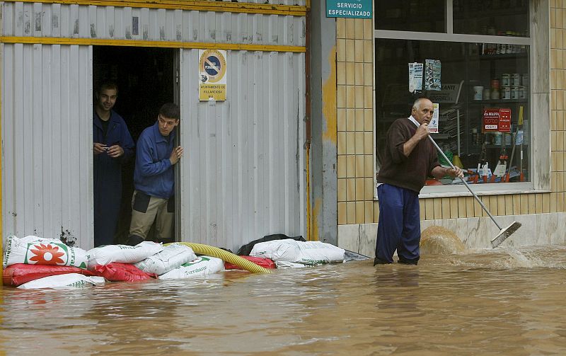 Un grupo de hombres protege con sacos de arena la entrada de un garaje, amenazada por una riada que ha inundado una de las calles de Villaviciosa, Asturias.