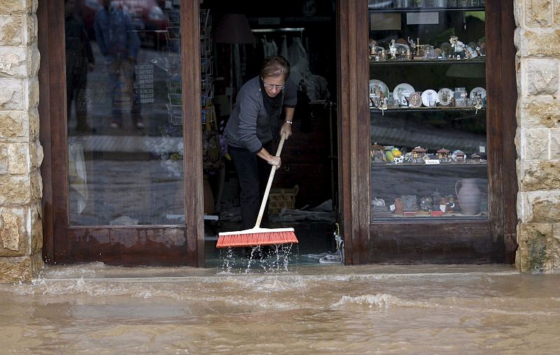 Una mujer trata de achicar el agua que ha inundado su tienda, en el municipio asturiano de Villaviciosa, uno de los más afectados por las últimas lluvias que han caído sobre la región.