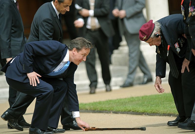 Cameron se agacha a por un bastón que ha resbalado de las manos de uno de los veteranos, durante el homenaje a las combatientes de los nazis de la segunda guerra mundial.